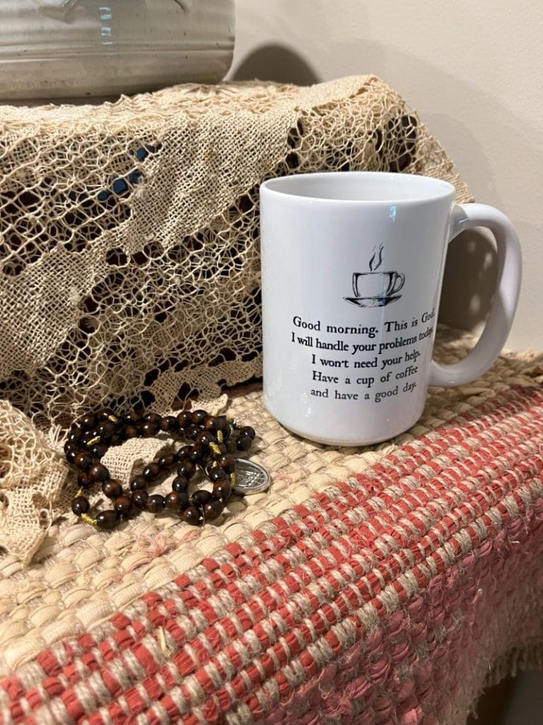 Coffee cup with surrender phrase, and rosary beads on a table