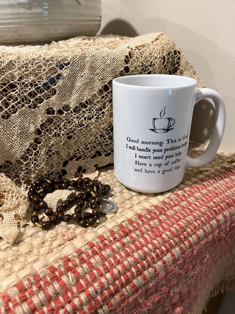 Coffee cup with surrender phrase, and rosary beads on a table