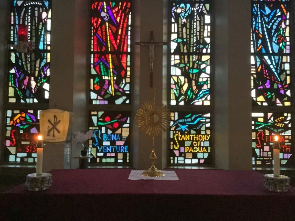 Eucharist in Monstrance, stained glass windows behind, also a tabernacle