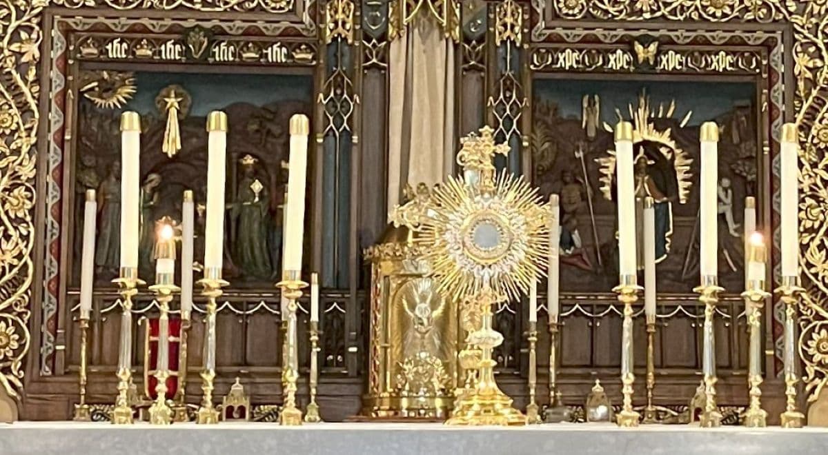 Eucharist in Monstrance on the altar in front of tabernacle surrounded by white pillar candles